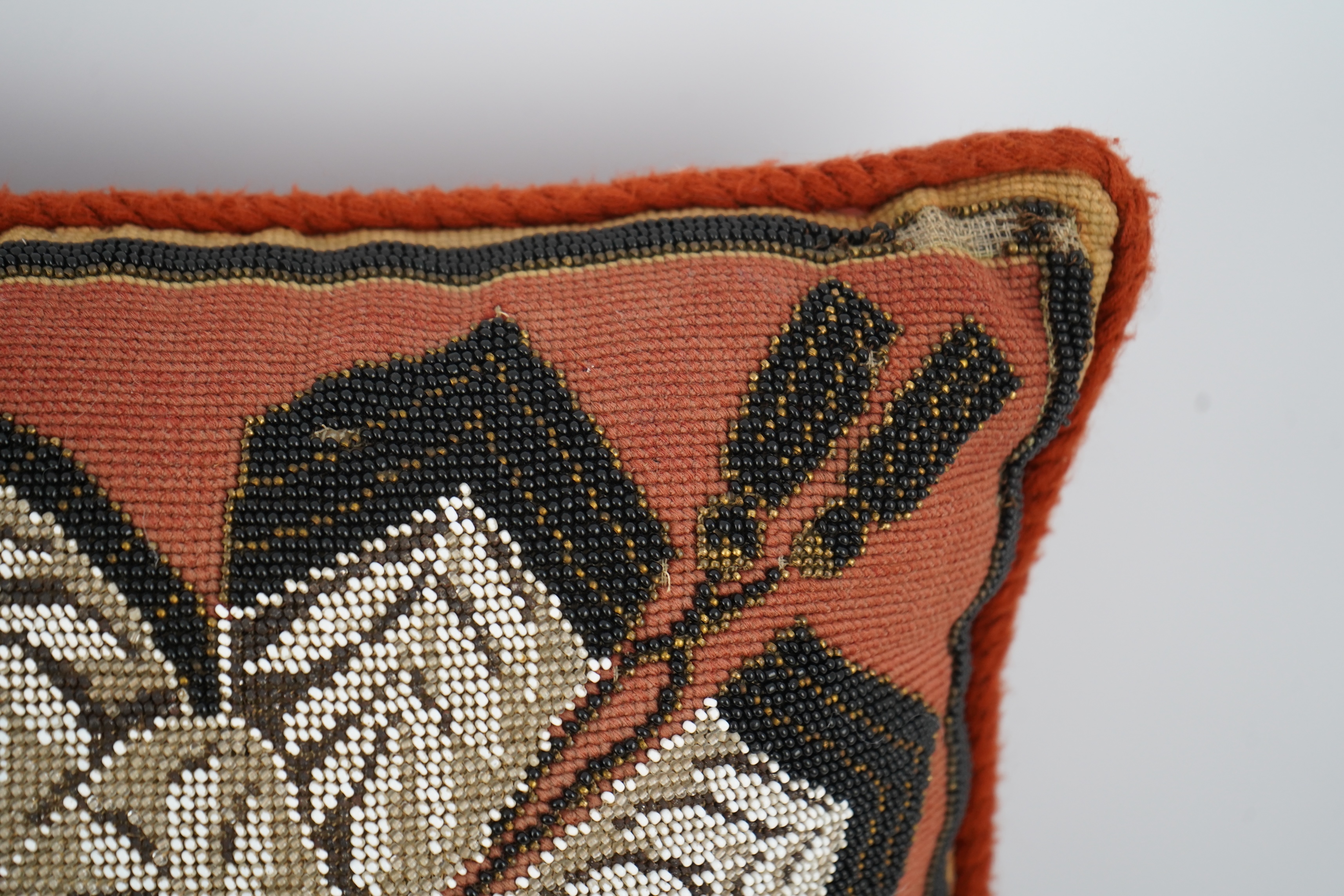 A 19th century Berlin bead worked cushion, the beadwork embroidered as a central rose, surrounded by an ornate tasseled swag, on a red wool worked background, 43cm x 45cm. Condition - some beadwork missing due to age and